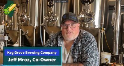A man is sitting in front of a brewery with a sign that says keg grove brewing company.