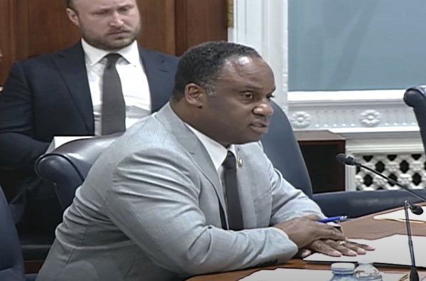A man in a suit and tie is sitting at a table in front of a microphone.