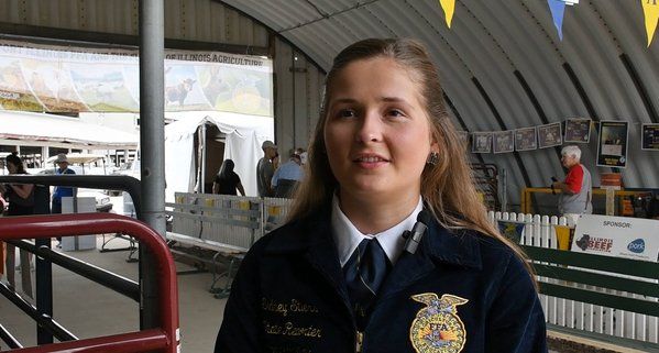 A woman in a ffa uniform is standing in a barn