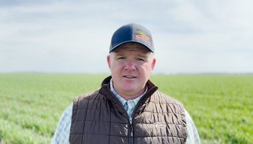 A man wearing a hat and vest is standing in a field of green grass.
