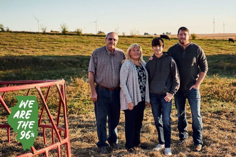 A family is posing for a picture in a field with cows in the background.