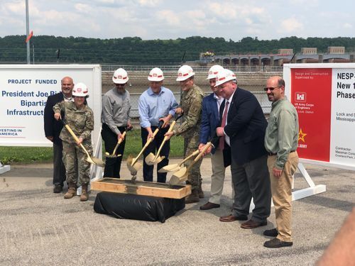 A group of people are holding shovels in front of a sign.