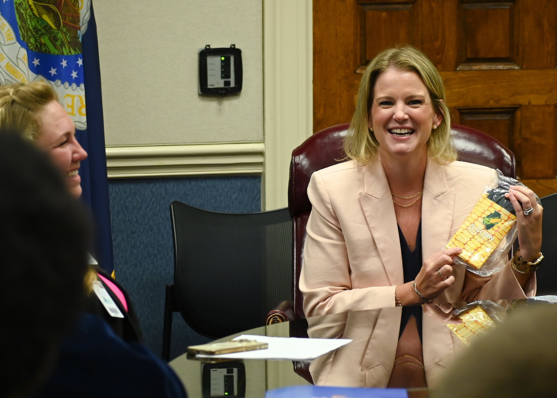 Woman in pink suit holding snack, smiling, in a meeting.