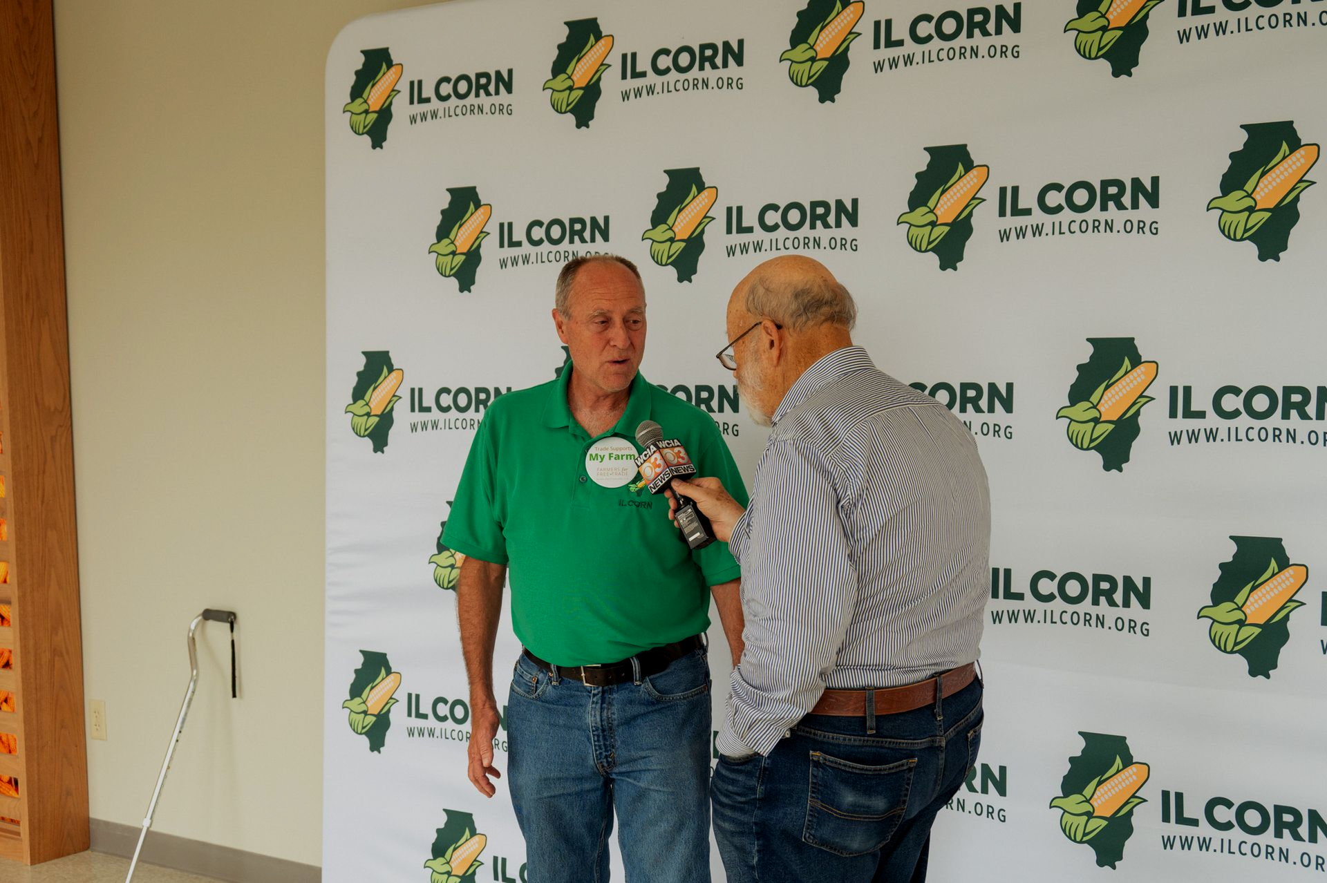 Man in green shirt being interviewed in front of IL Corn backdrop.