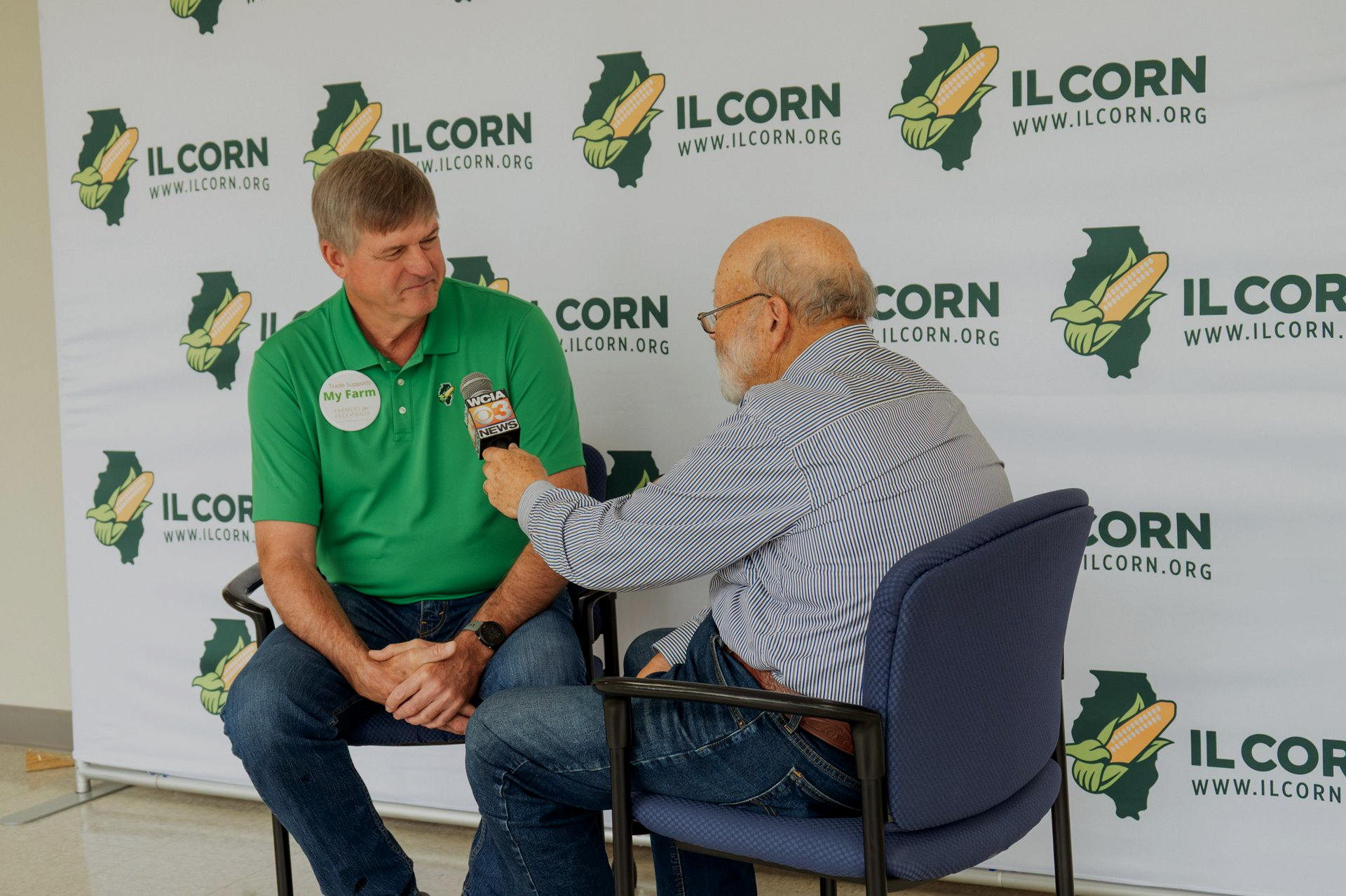Man in green shirt interviewed by man holding a microphone, against a