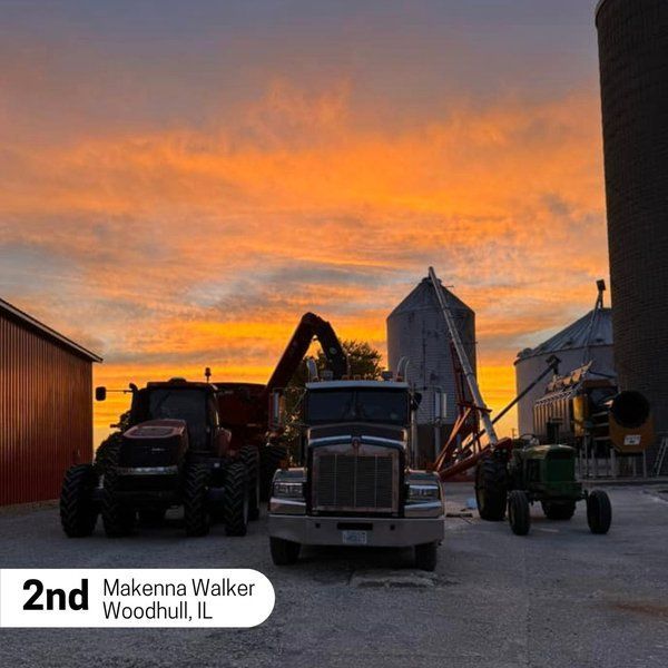 Tractors are parked in a parking lot with a sunset in the background
