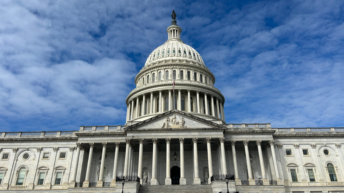 U.S. Capitol building under a partly cloudy blue sky, centered front facade with white dome and columns