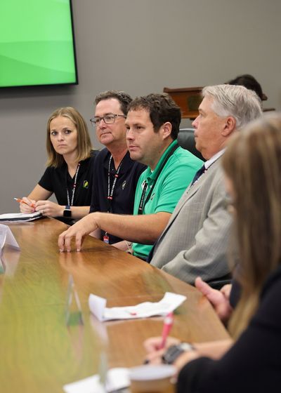 A group of people are sitting at a table in front of a green screen