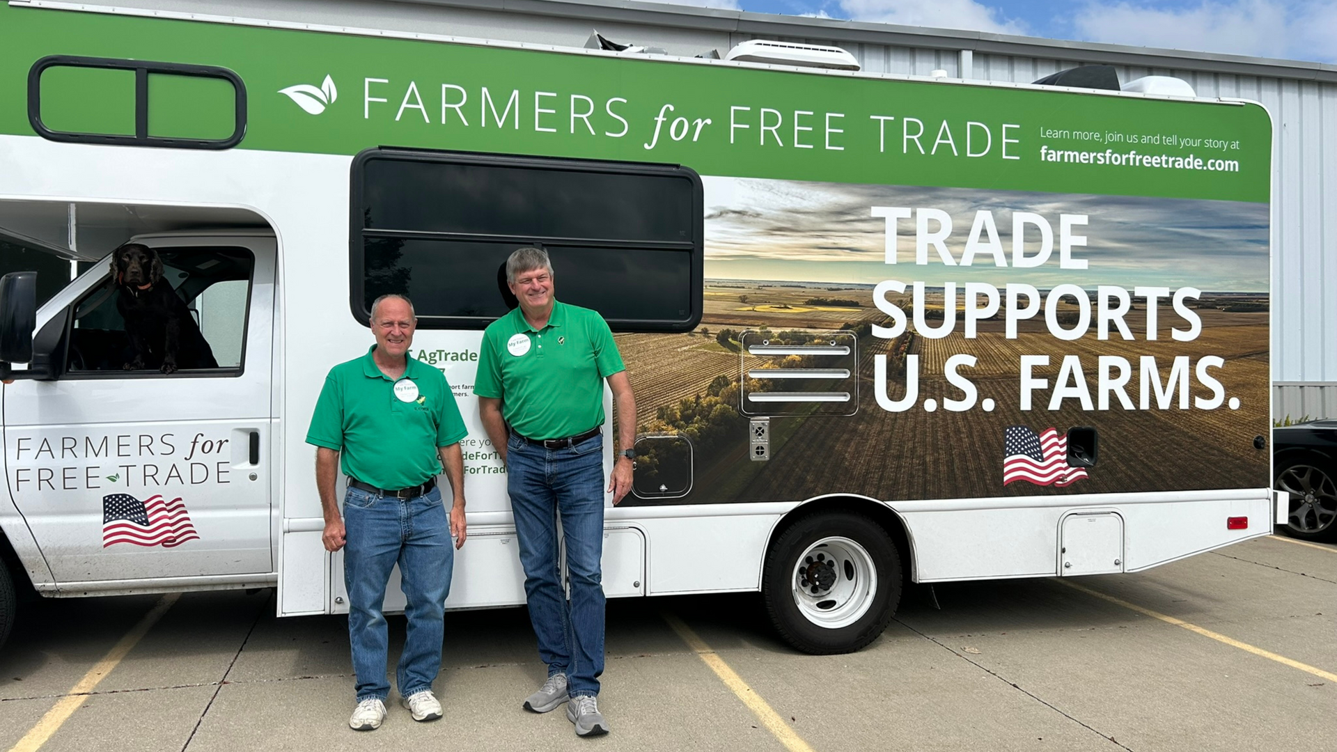 Two men in green shirts stand beside a bus with 