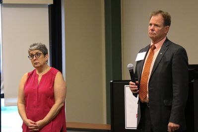 A man in a suit and tie is holding a microphone while standing next to a woman in a red shirt.