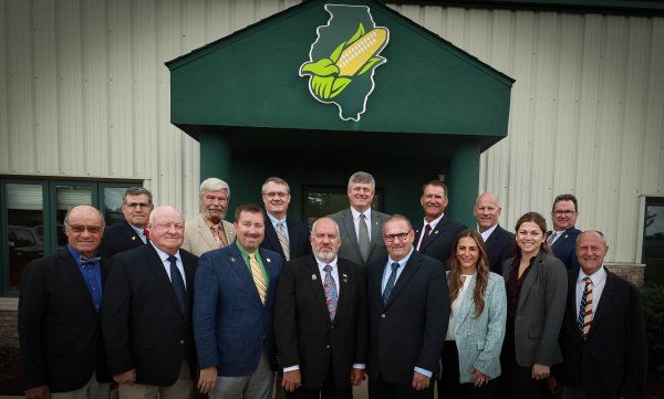 A group of people are posing for a picture in front of a building with a corn on it.