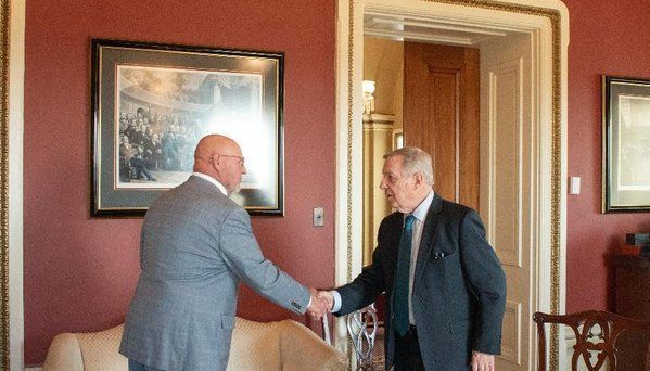 Two men in suits are shaking hands in a living room.