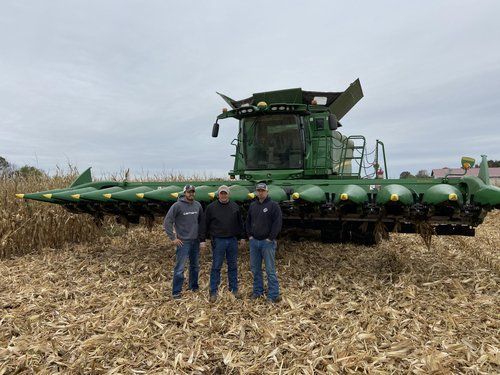 Three men are standing in a field in front of a combine harvester.