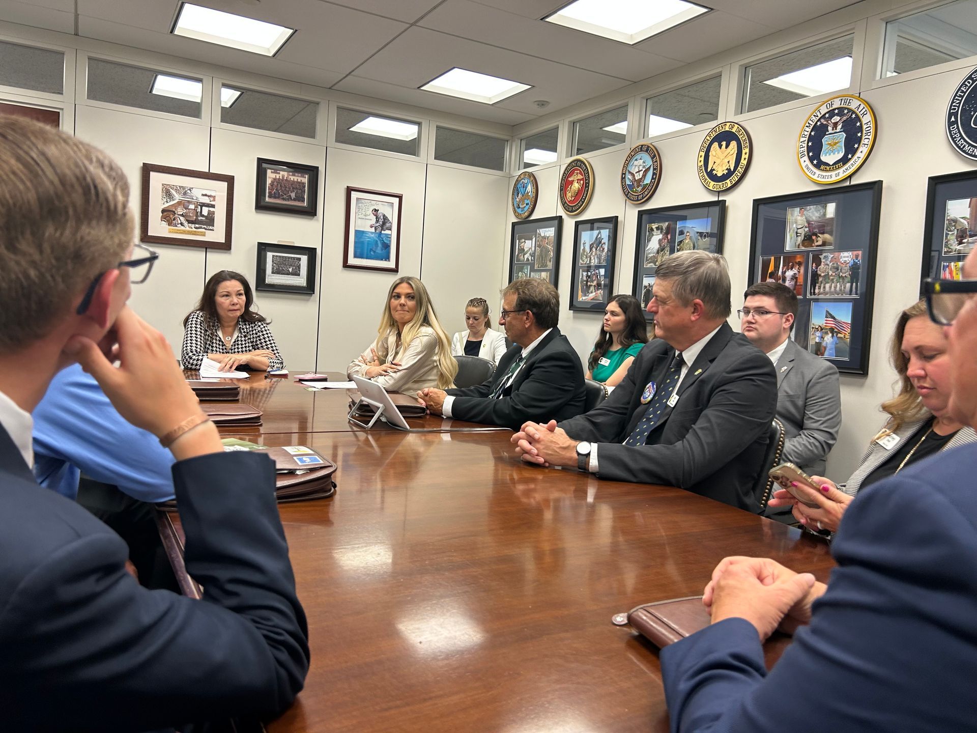 A group of people seated around a large table in an office, engaged in a meeting.