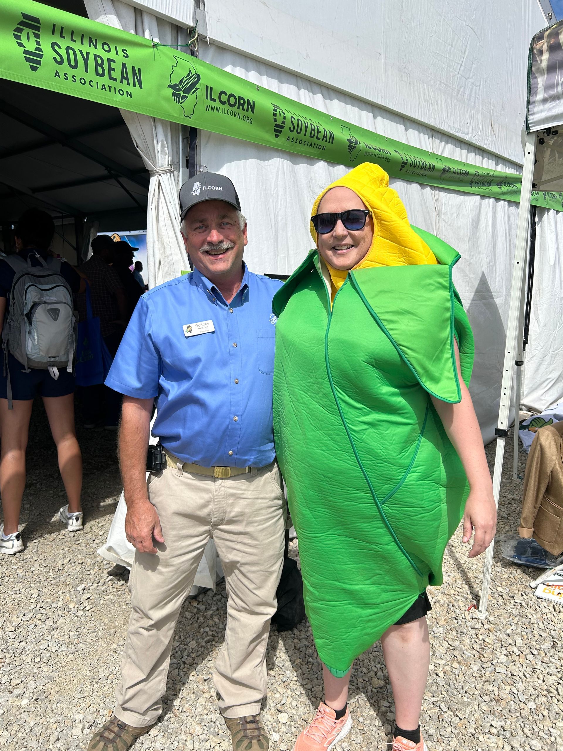 Man and woman in a corn costume at the Illinois Soybean Association event. They are smiling, outside a tent.