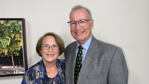 A man and a woman are posing for a picture in front of a painting.