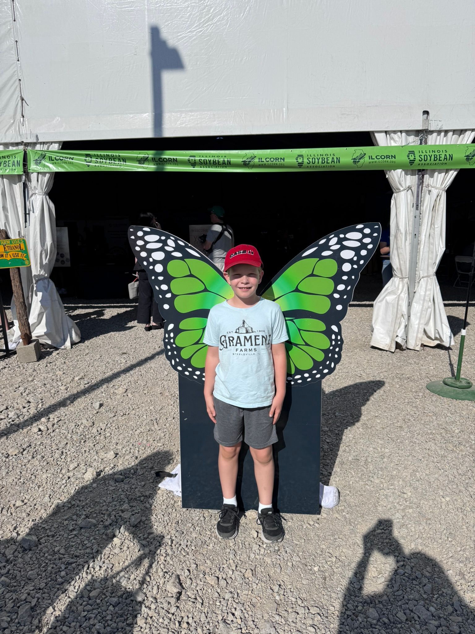 Boy with a red cap poses in front of green butterfly wings, under a white tent.