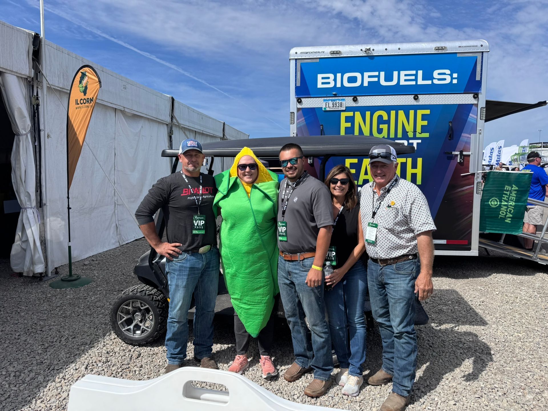 Group of five people, one dressed as corn, posing near a golf cart with a 