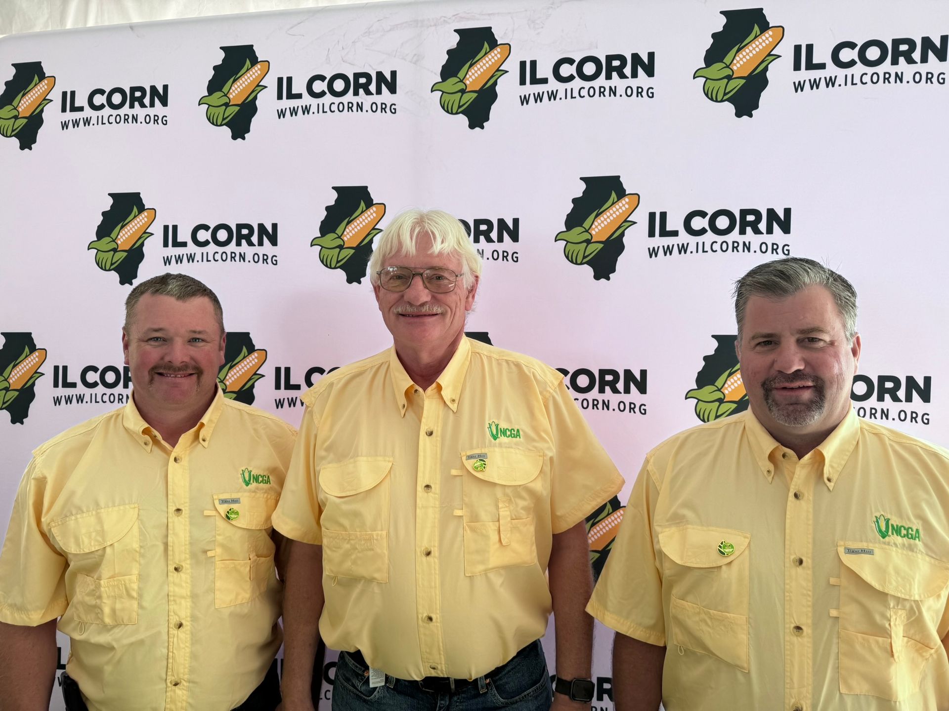 Three men in yellow shirts pose in front of an 