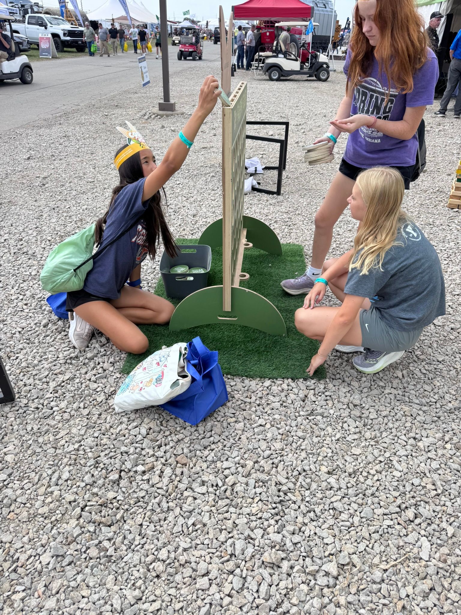 Three young women playing a ladder toss game outdoors on a gravel surface.