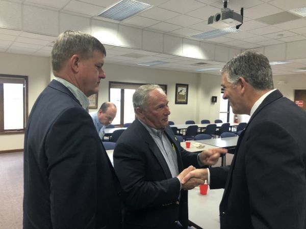 Three men in suits are standing in a room talking to each other