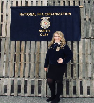 A woman stands in front of a national ffa organization north clay banner