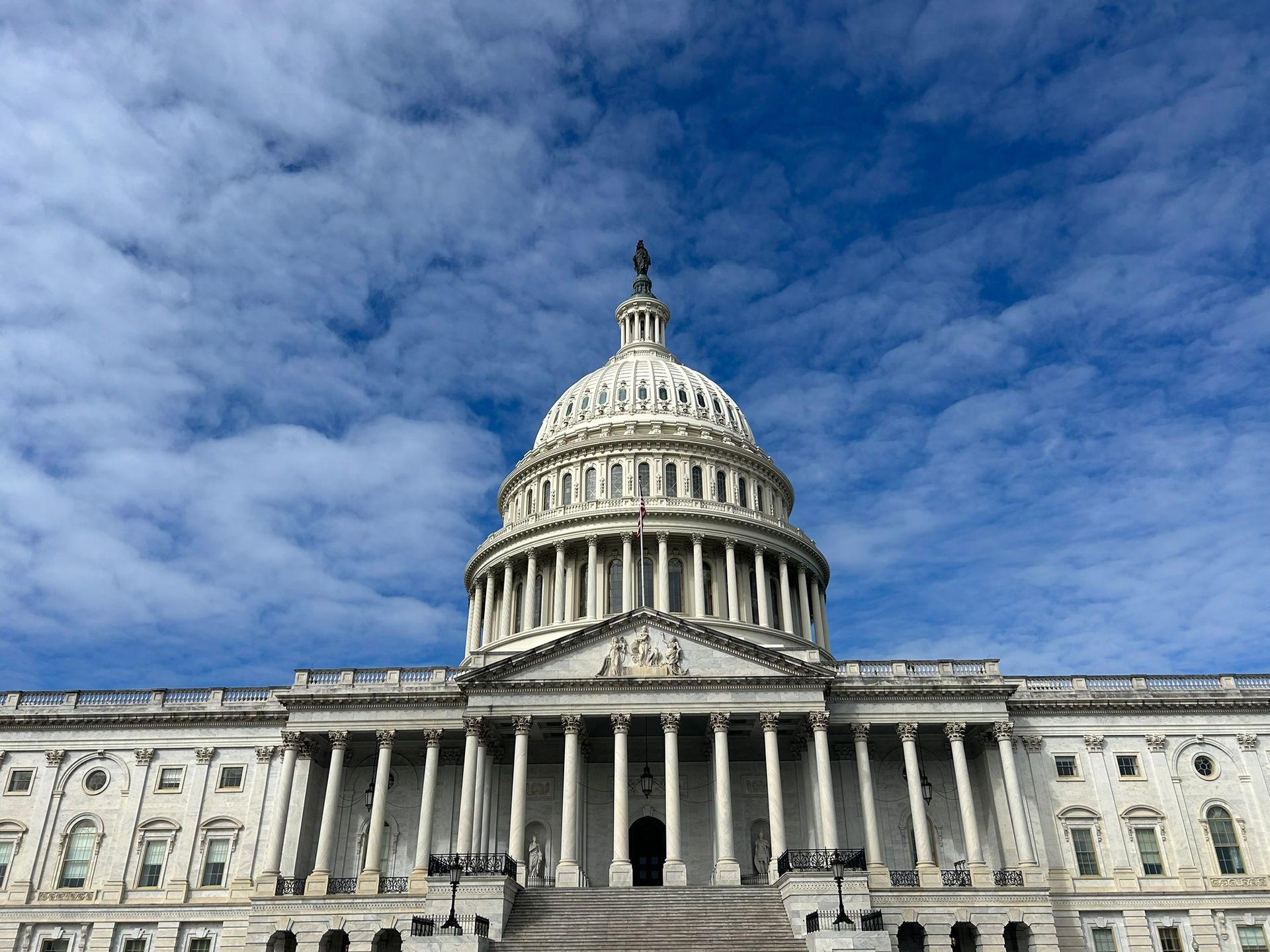 The United States Capitol building featuring its iconic white dome against a bright blue sky with scattered clouds.