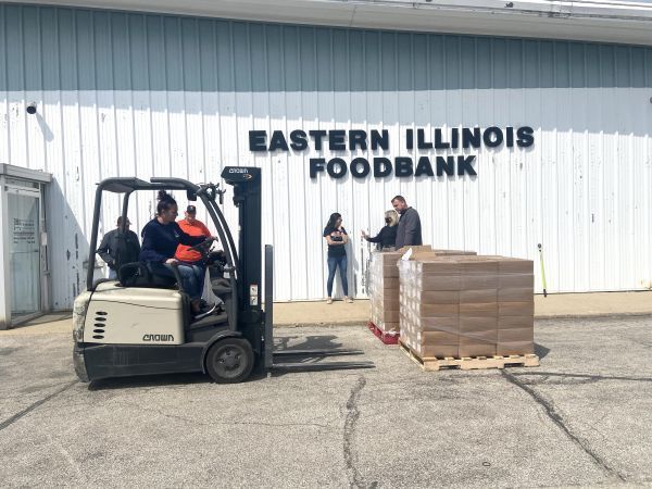 A man is driving a forklift in front of a building that says eastern illinois foodbank.