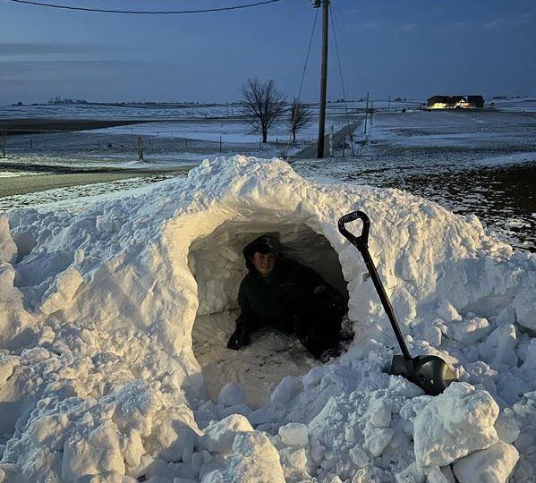 A man is crawling out of an igloo in the snow