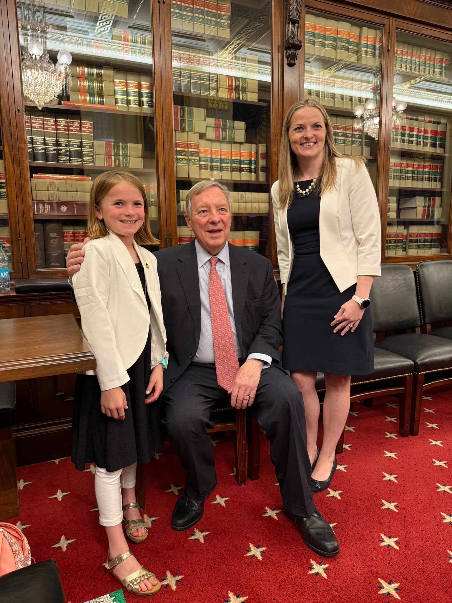 A man in a suit and tie is sitting next to two women in a library.