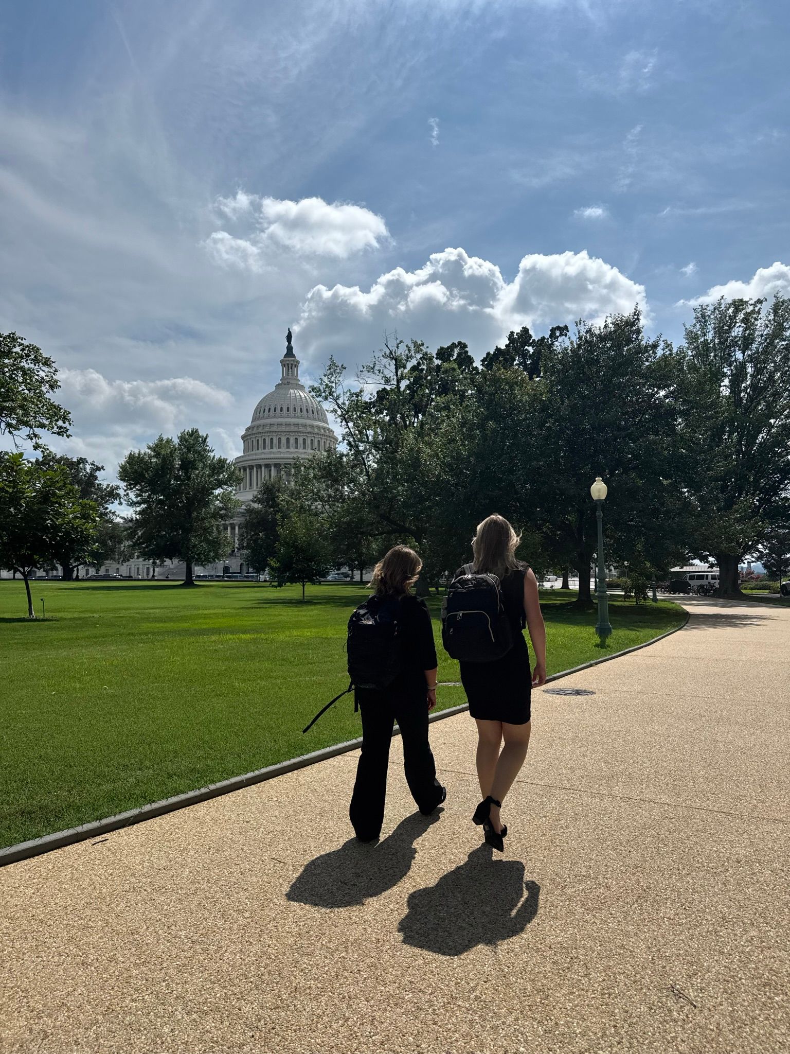 Two people walk towards the US Capitol building on a sunny day.