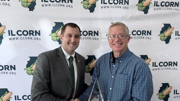 Two men are shaking hands in front of a banner that says il corn