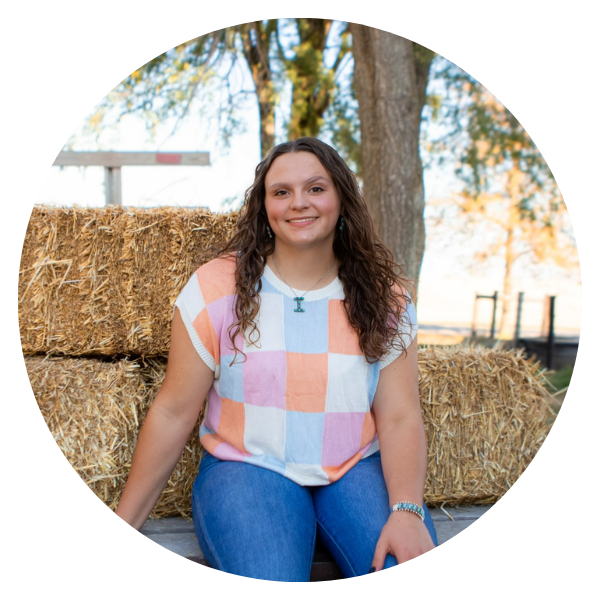 A woman in a plaid shirt is sitting in front of hay bales
