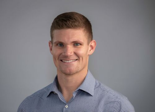 A man in a blue and white checkered shirt is smiling for the camera.