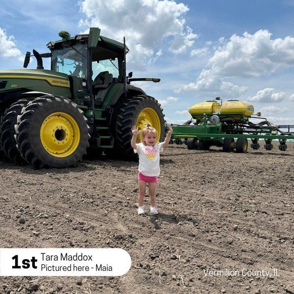 A little girl is standing in front of a john deere tractor