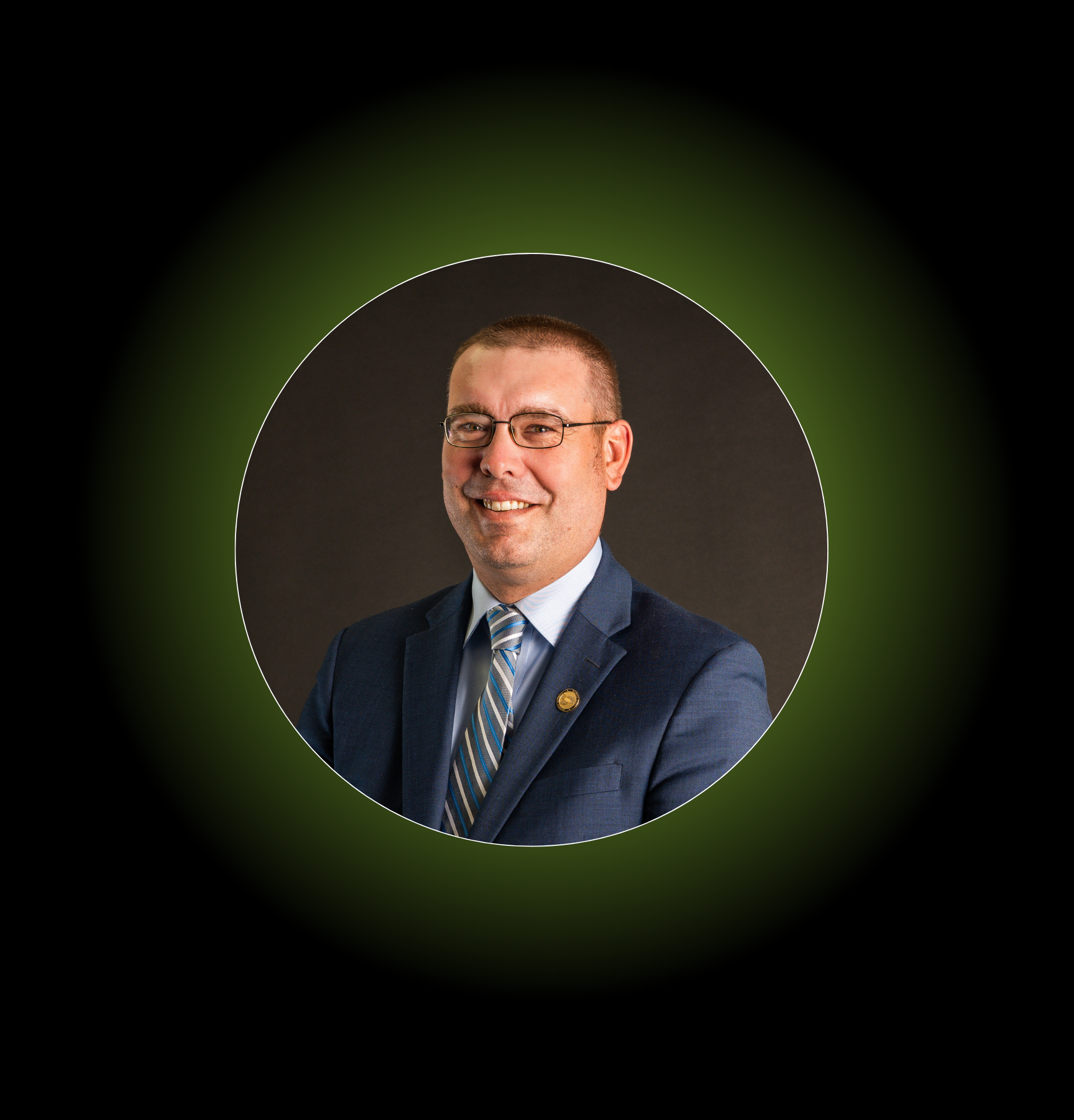 Man in suit and glasses smiles, set in an illuminated green-tinted circle on a black background.