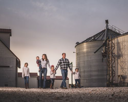 A family is walking in front of a grain silo on a farm.