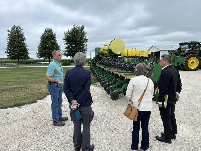 A group of people are standing in front of a john deere tractor.