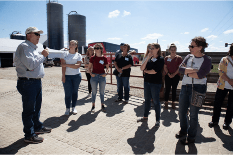 A group of people are standing in a circle in front of a farm.