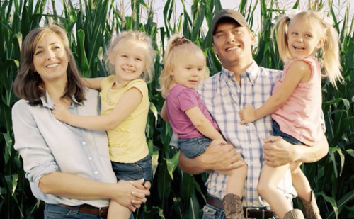 A family is posing for a picture in front of a corn field.
