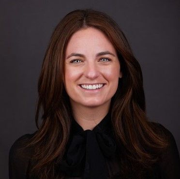 A woman with long brown hair is wearing a black shirt and smiling.