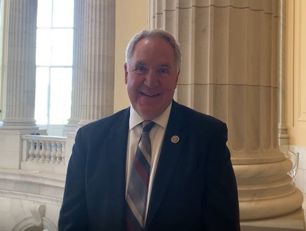 A man in a suit and tie is smiling in front of columns