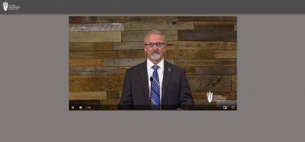 A man in a suit and tie is standing in front of a wooden wall.