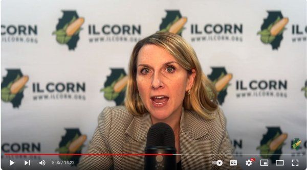 A woman is speaking into a microphone in front of a banner that says ilcorn