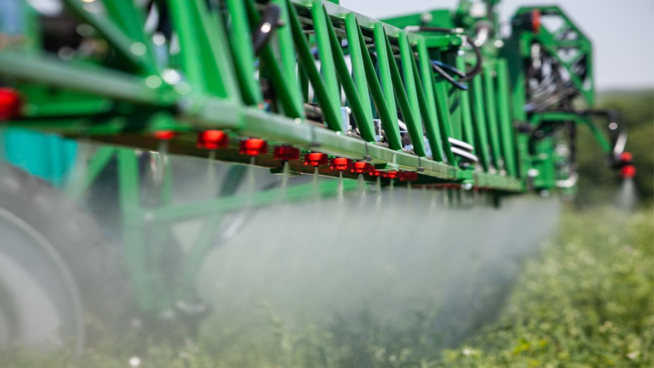 Green agricultural sprayer applying chemicals to crops.