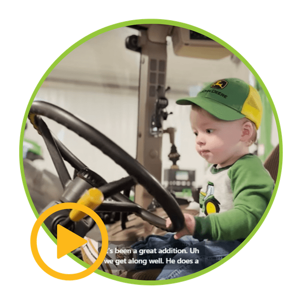 A baby wearing a john deere hat is driving a tractor