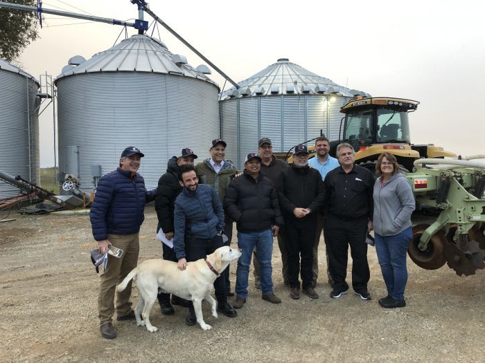 A group of people standing in front of a tractor and silos