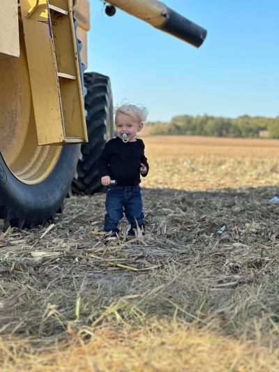 A little boy is standing in a field next to a tractor.