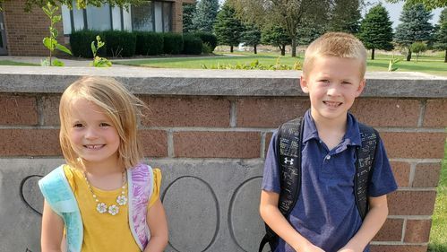 A boy and a girl are standing next to each other in front of a brick wall.