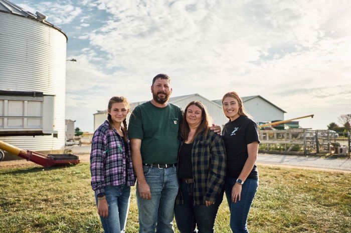 A family is posing for a picture in front of a silo on a farm.